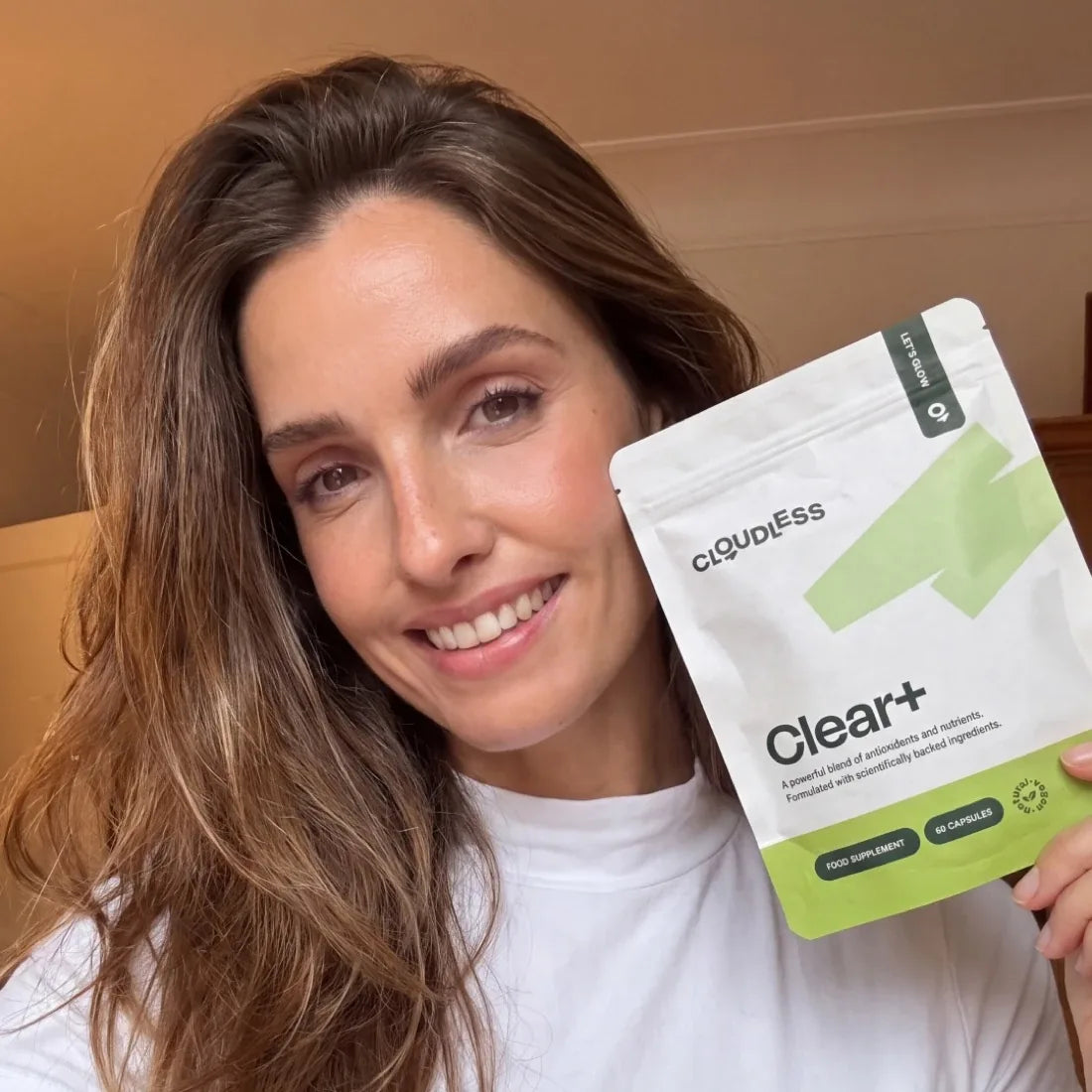 Eine lächelnde Frau mit reiner Haut hält Clear+ in der Hand